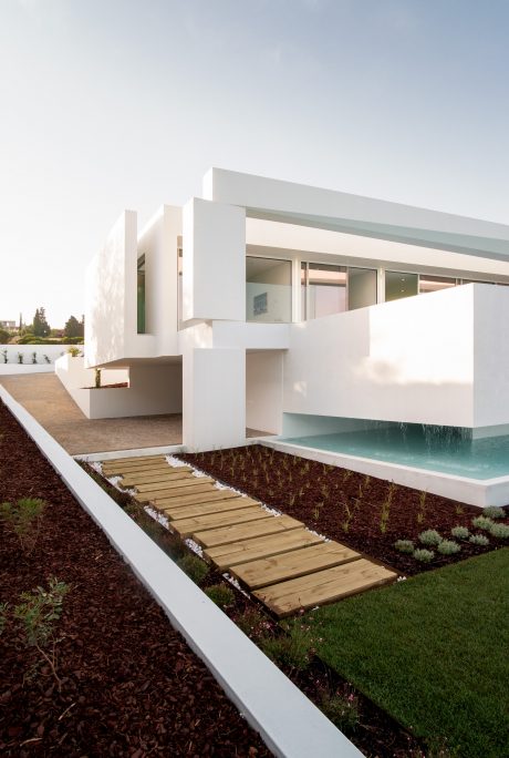 Modern and minimalist white exterior with clean lines, wooden walkway, and pool.