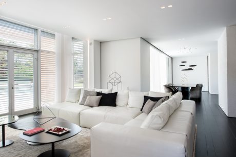 Spacious, light-filled living room with white modular sofa, geometric wall decor, and large windows.
