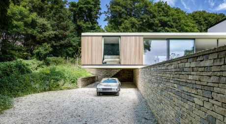 Sleek, modern structure built into a lush, wooded landscape with a car parked beneath.