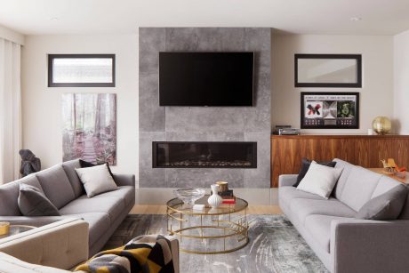 Sleek modern living room with concrete fireplace, wood furniture, and gold accents.