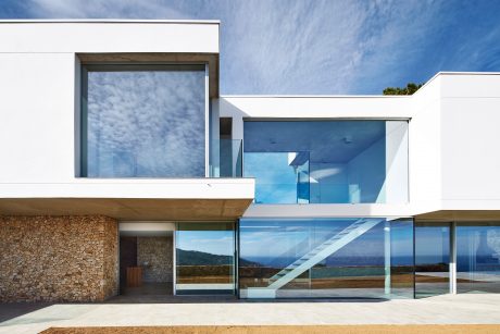 Modern seaside villa with glass walls, stone façade, and open-plan design showcasing the scenic ocean view.