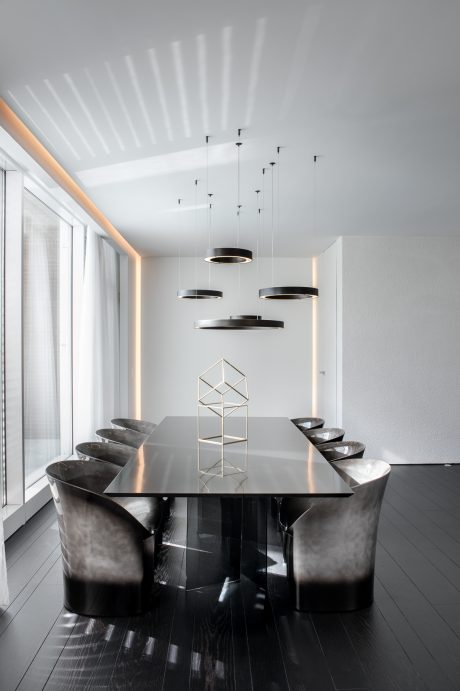 A modern, minimalist dining room with a sleek, black table and pendant lighting.