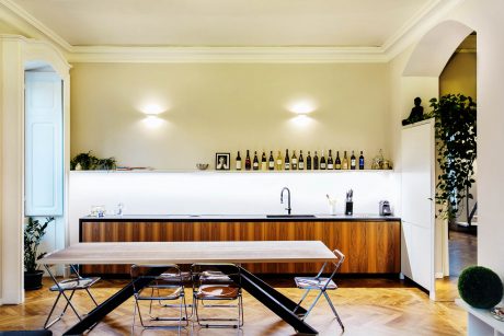 A spacious, modern kitchen with wooden cabinetry, floating shelves, and a large dining table.