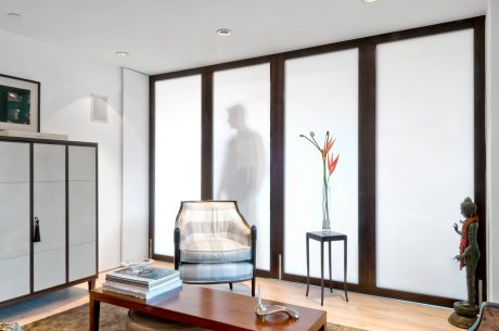 Modern living room with floor-to-ceiling wooden window frames, plush chair, and decorative accents.