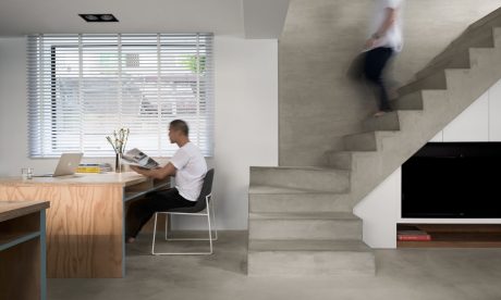 Modern minimalist workspace with concrete staircase, wooden desk, and person working.