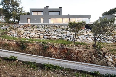 Modern, multi-story residence with stone exterior and large windows set atop a rocky hillside.