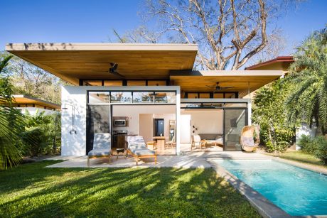 A modern, open-concept house with a wooden roof, sliding glass doors, and a private pool.