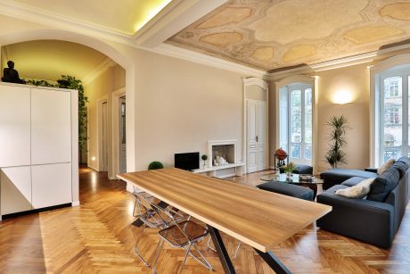 Ornate ceiling with intricate patterns, modern furnishings, and expansive windows in this grand room.