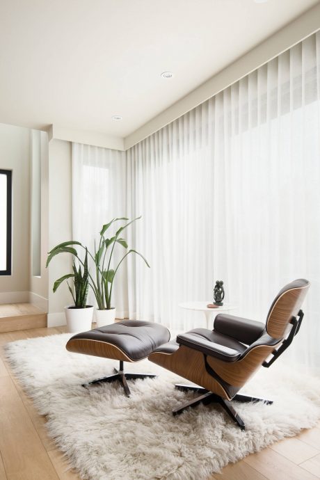 Modern, minimalist living room with wooden Eames-style lounge chair, shag rug, and potted plants.