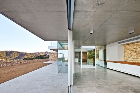 Expansive, modern interior with concrete ceiling, glass walls, and stone accent wall.