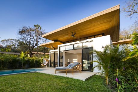 Striking modern design with wood accents, expansive windows, and lush tropical landscaping.