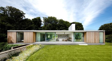 A contemporary, single-story house with expansive glass walls, wood accents, and a lush garden.