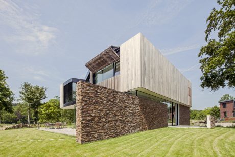 A modern, geometric building with wood siding and stone walls surrounded by green lawn.