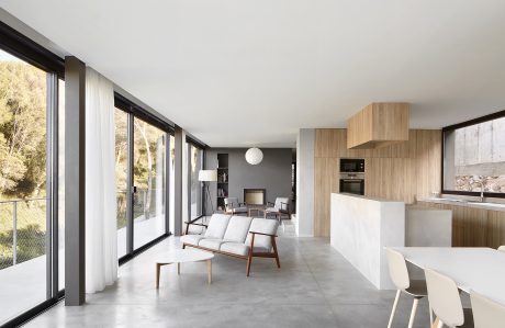 Modern, open-concept living space with floor-to-ceiling windows, concrete floors, and wood-paneled cabinetry.