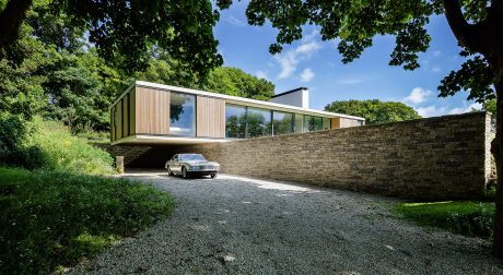 A modern, minimalist home with a wooden exterior and glass walls, surrounded by lush greenery.