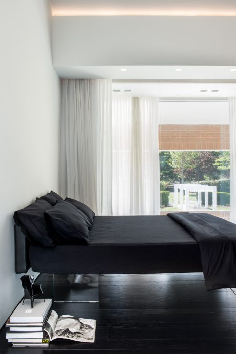 Minimalist bedroom with sleek black furniture, white curtains, and a view of the outdoors.