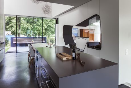 Sleek, modern kitchen with glass walls, pendant lights, and a dark countertop island.