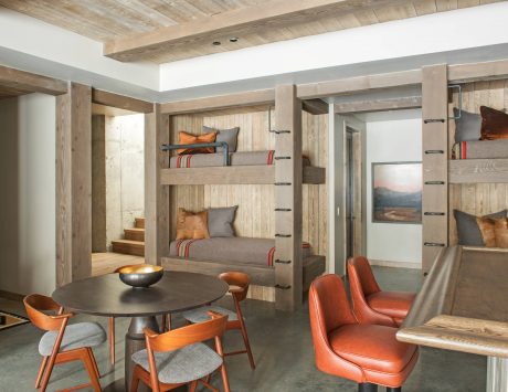 Rustic, cozy cabin interior with wood-paneled walls, bunk beds, and vibrant orange chairs.