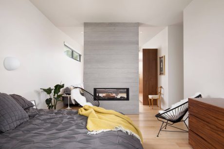 Minimalist bedroom with a wooden accent wall, fireplace, and modern furnishings.