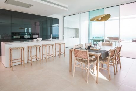Sleek, modern kitchen and dining area with glass walls, natural rattan seating.