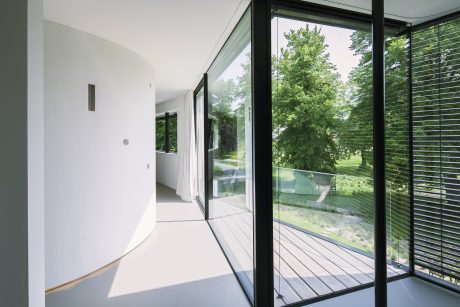 Modern hallway with large glass walls overlooking a lush green landscape.