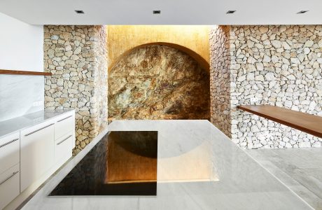 A modern kitchen with stone walls, a stone arch, and a marble countertop.