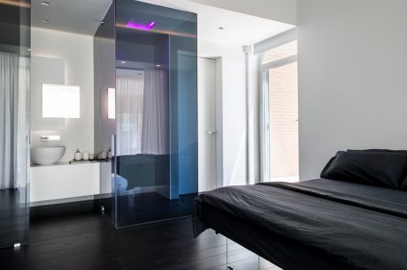 Sleek, modern bedroom with glass-enclosed shower, dark wood floors, and purple lighting.