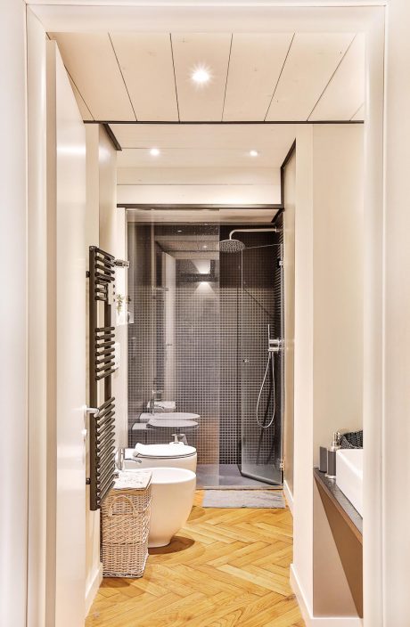 A modern bathroom with sleek lighting, tiled walls, and herringbone wood flooring.