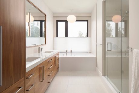 Spacious, modern bathroom with wooden vanity, white countertops, and large windows.