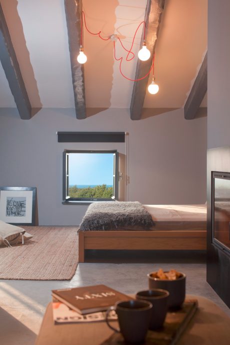 Cozy bedroom with modern lighting, wooden beams, and scenic window view.