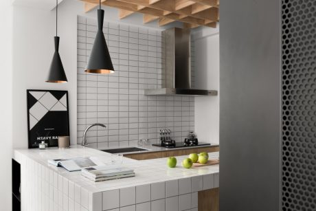 A modern kitchen with white tiles, wooden beams, and black pendant lights.