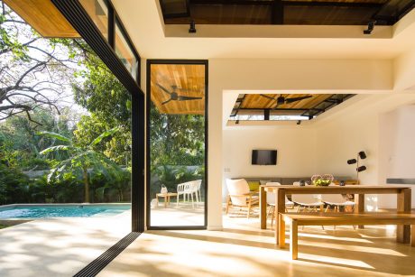 Open, airy living space with wooden beams, pool views, and minimalist furnishings.
