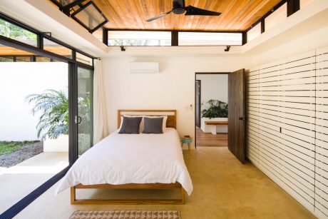 A spacious and modern bedroom with wooden ceiling, sliding glass doors, and concrete floors.