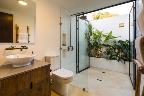 An elegant bathroom with a glass-enclosed shower, wooden vanity, and lush greenery outside.