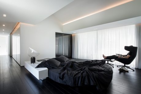 Minimalist bedroom with sleek black furniture, large windows, and recessed lighting.