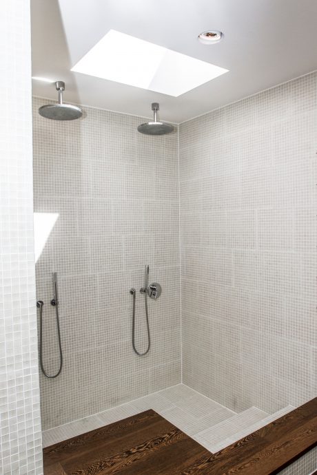 Modern, minimalist shower room with recessed lighting, mosaic tiling, and wood-grain flooring.