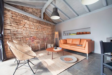 Rustic interior with stone wall, orange sofa, woven chair, and modern lighting.