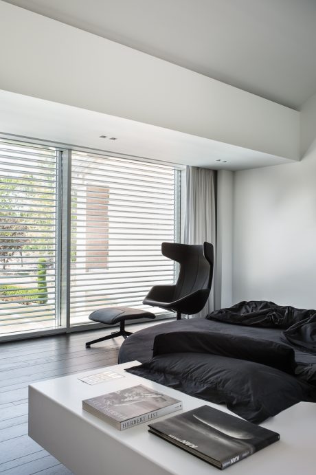 Minimalist bedroom with floor-to-ceiling windows, modern chair, and monochromatic decor.