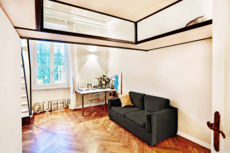 A cozy room with hardwood floors, wooden beams, and a black sofa, accented by decorative elements.