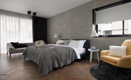 Spacious modern bedroom with gray walls, wooden flooring, and furnishings in neutral colors.