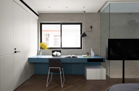 A modern and minimalist bedroom with sleek built-in desk, wood flooring, and glass walls.