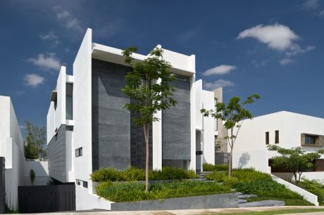 Modern, angular white building with lush greenery and minimal landscaping against a blue sky.