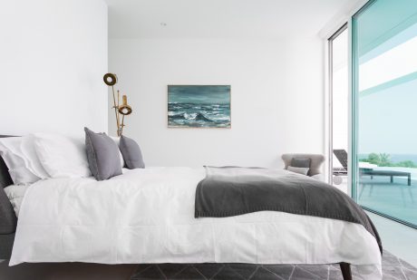 Spacious bedroom with modern furniture, coastal artwork, and floor-to-ceiling windows.