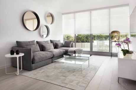 Modern, minimalist living room with gray sofa, glass coffee table, and circular mirrors on the wall.