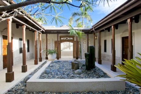 Serene tropical courtyard with wooden pavilion, stone features, and lush greenery.