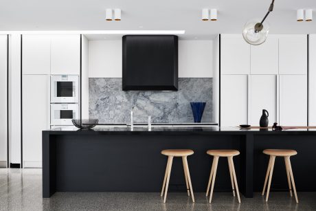 Modern kitchen with sleek black cabinetry, marble backsplash, and wooden bar stools.