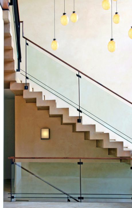 Sleek modern staircase with wooden treads and glass balustrade, accented by hanging lamps.