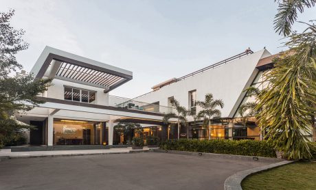 Modern tropical architectural design with expansive glass walls, overhanging roofs, and lush landscaping.