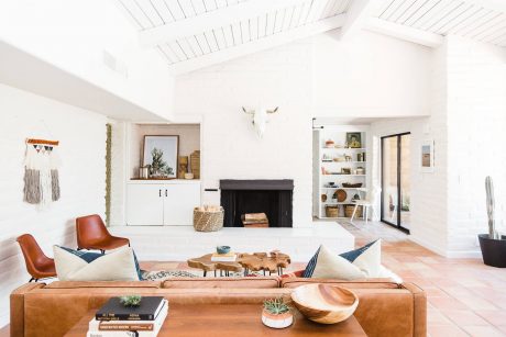 Bright, open-concept living room with white walls, wood beams, and a stone fireplace.