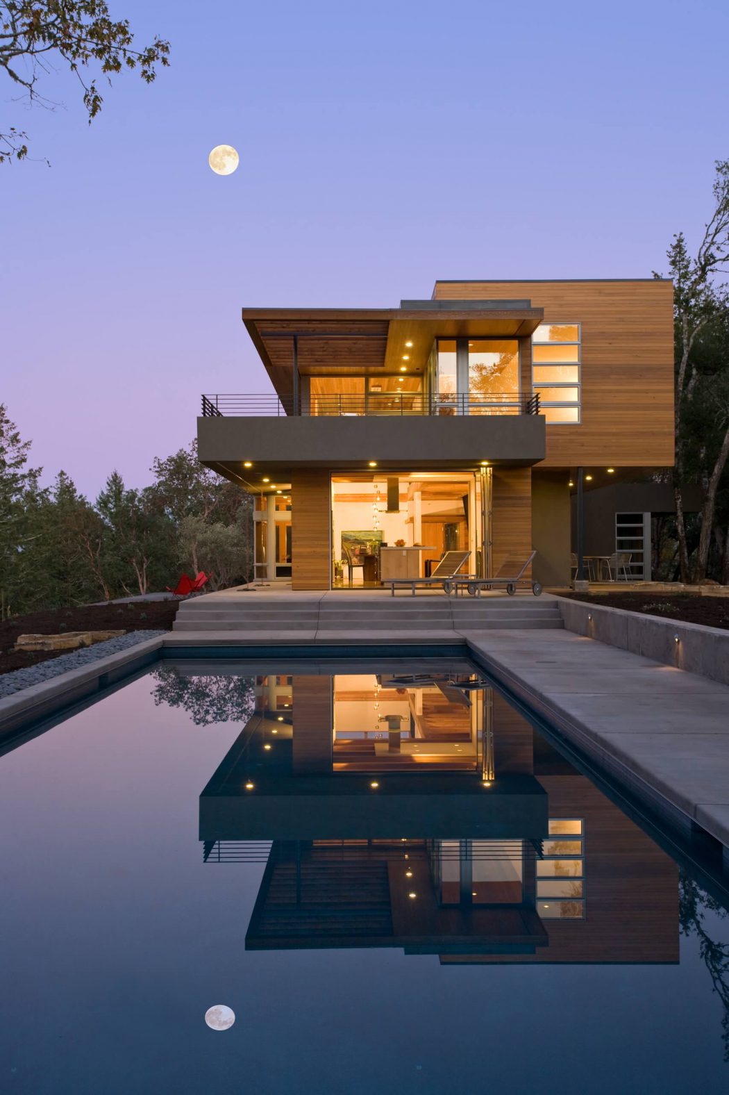 Modern wooden and glass home with a reflection pool, elevated deck, and full moon.